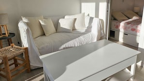 Et minimalistisk rum med en hvid sofa, et lille træbord og en seng med blomstret dyne.