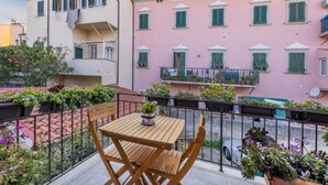 A balcony with a wooden table and chairs, potted plants, and a pink building with green shutters in the background. - La Barca Open Space - Goelba (Marciana Marina)