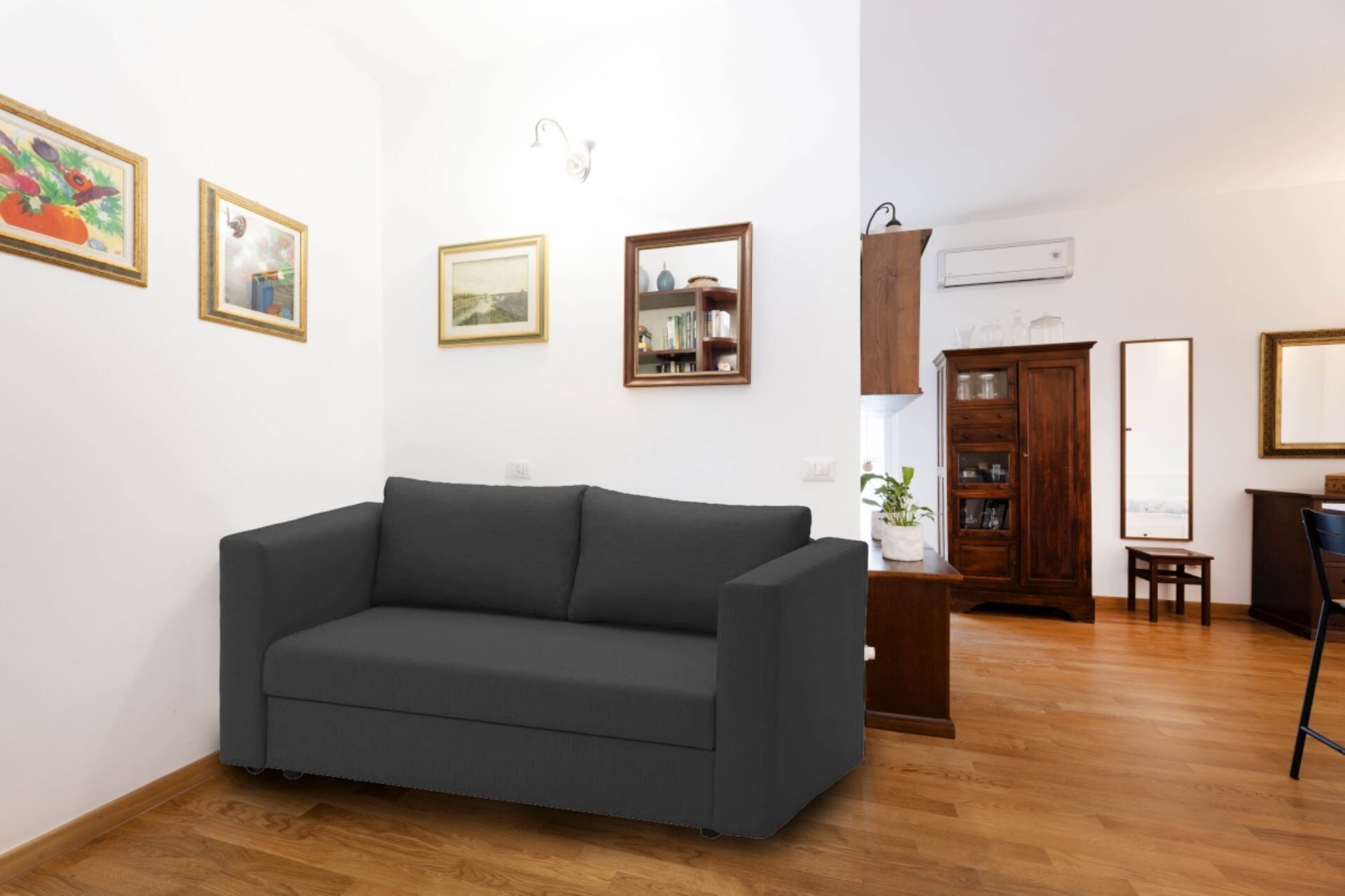 A living room with a dark grey sofa, wooden flooring, and a bookshelf.