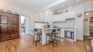 A modern kitchen with a central island, bar stools, white cabinetry, and a wooden floor. - La Barca Open Space - Goelba (Marciana Marina)