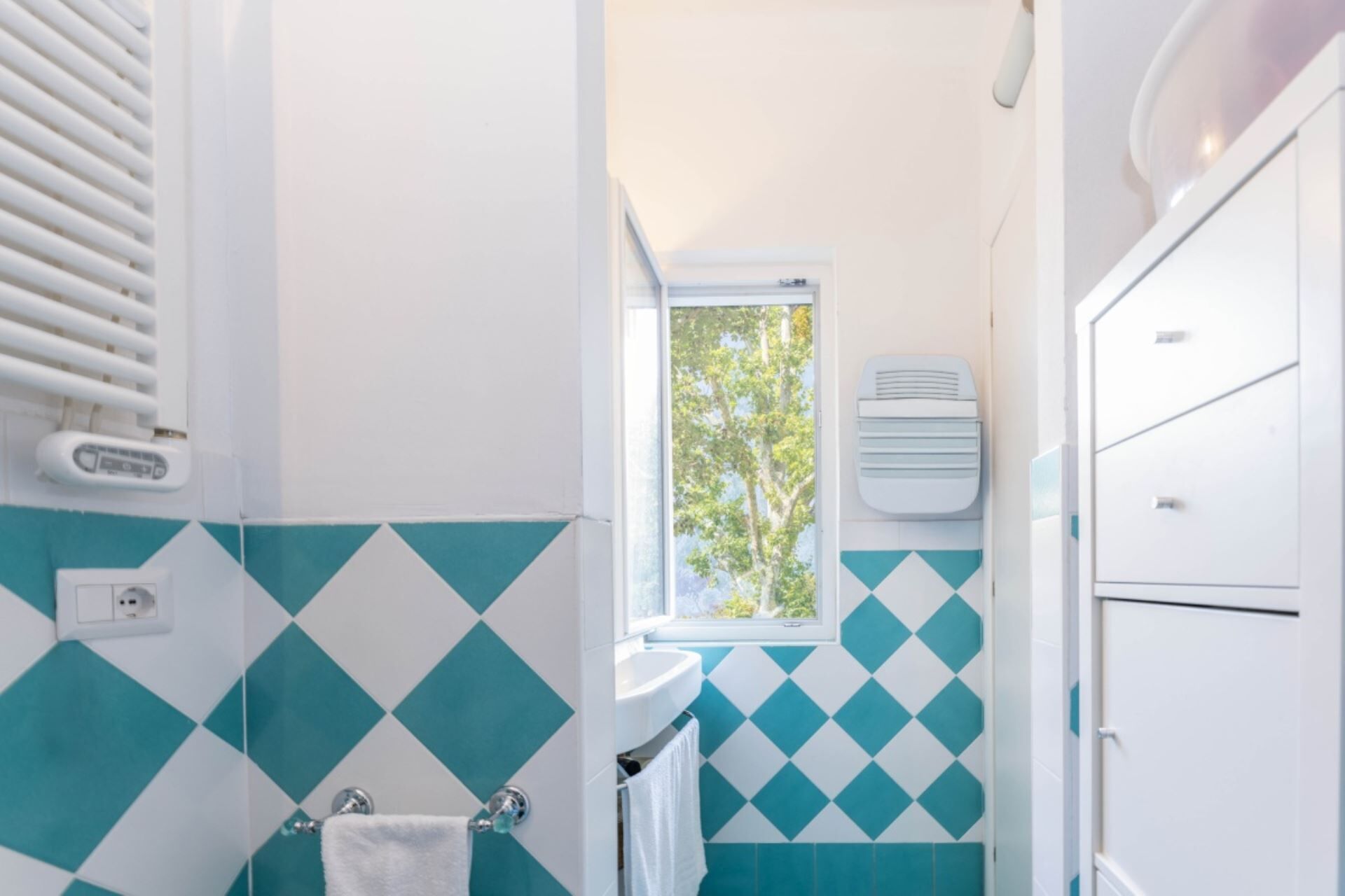 A bathroom with a window, a sink, a towel rack, and a heater.