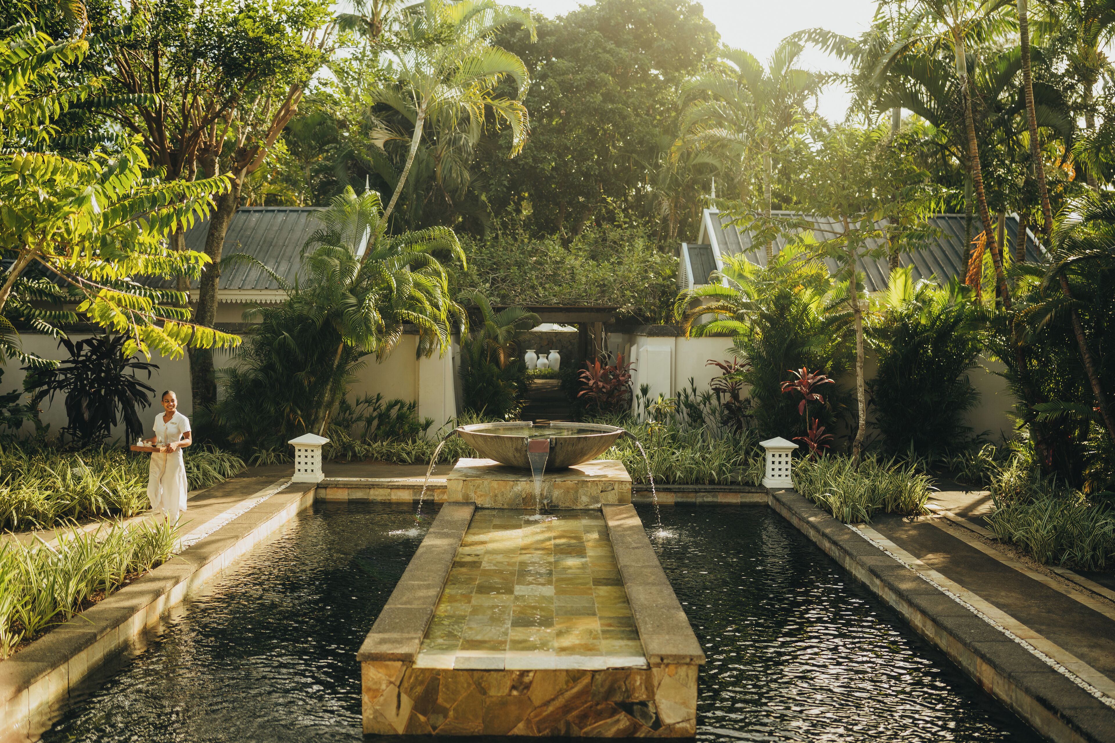 A serene garden with a central fountain, surrounded by lush greenery and a pathway.