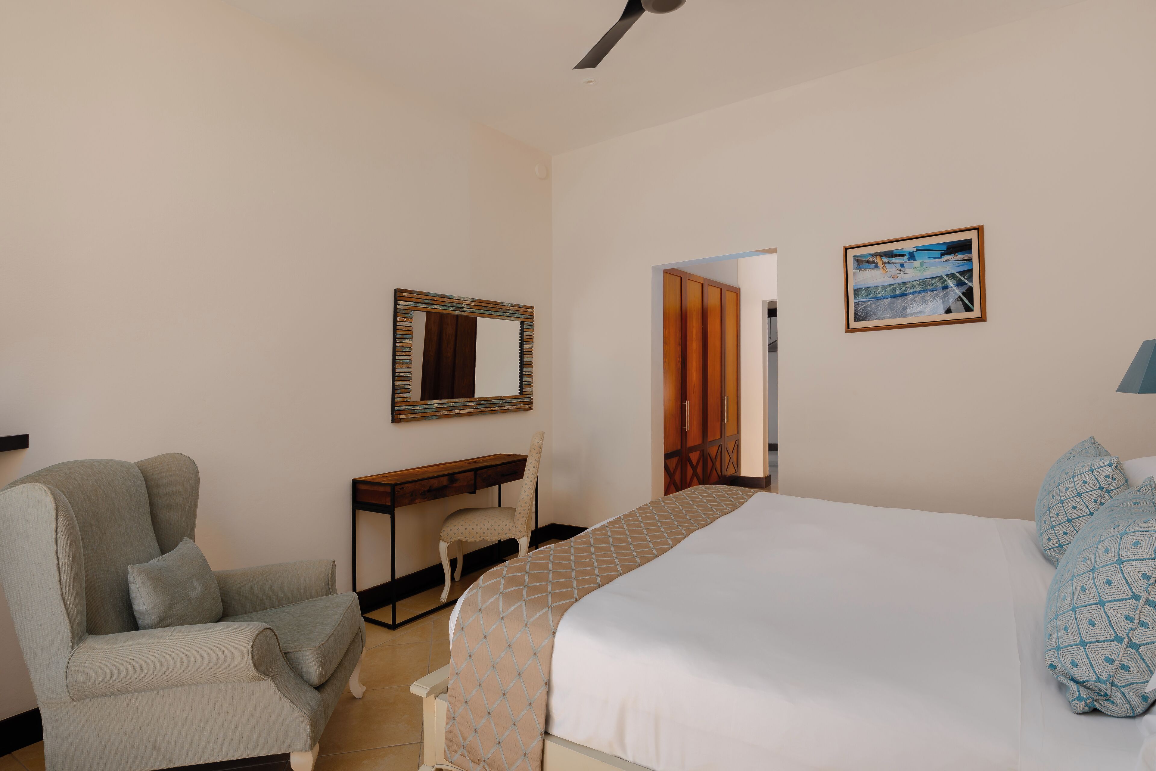 Habitación de hotel con una cama, una silla, un escritorio, un espejo y un cuadro en la pared.