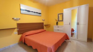 Een slaapkamer met een bed, een kledingkast, een nachtkastje, een spiegel en een aan de muur hangend schilderij.