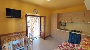 Een compacte leefruimte met een kitchenette, een eethoek en een aan de muur bevestigde televisie.