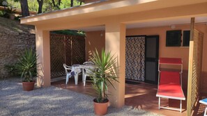 A covered outdoor seating area with a table and chairs, potted plants, and a red bench. - VILLA PINETA MARE - PIGNA 4 - VILLA PINETA MARE (Capoliveri)