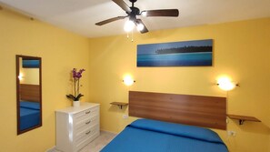 A bedroom with a bed, a ceiling fan, a dresser, a mirror, and a painting of a beach scene. - VILLA PINETA MARE - PIGNA 4 - VILLA PINETA MARE (Capoliveri)