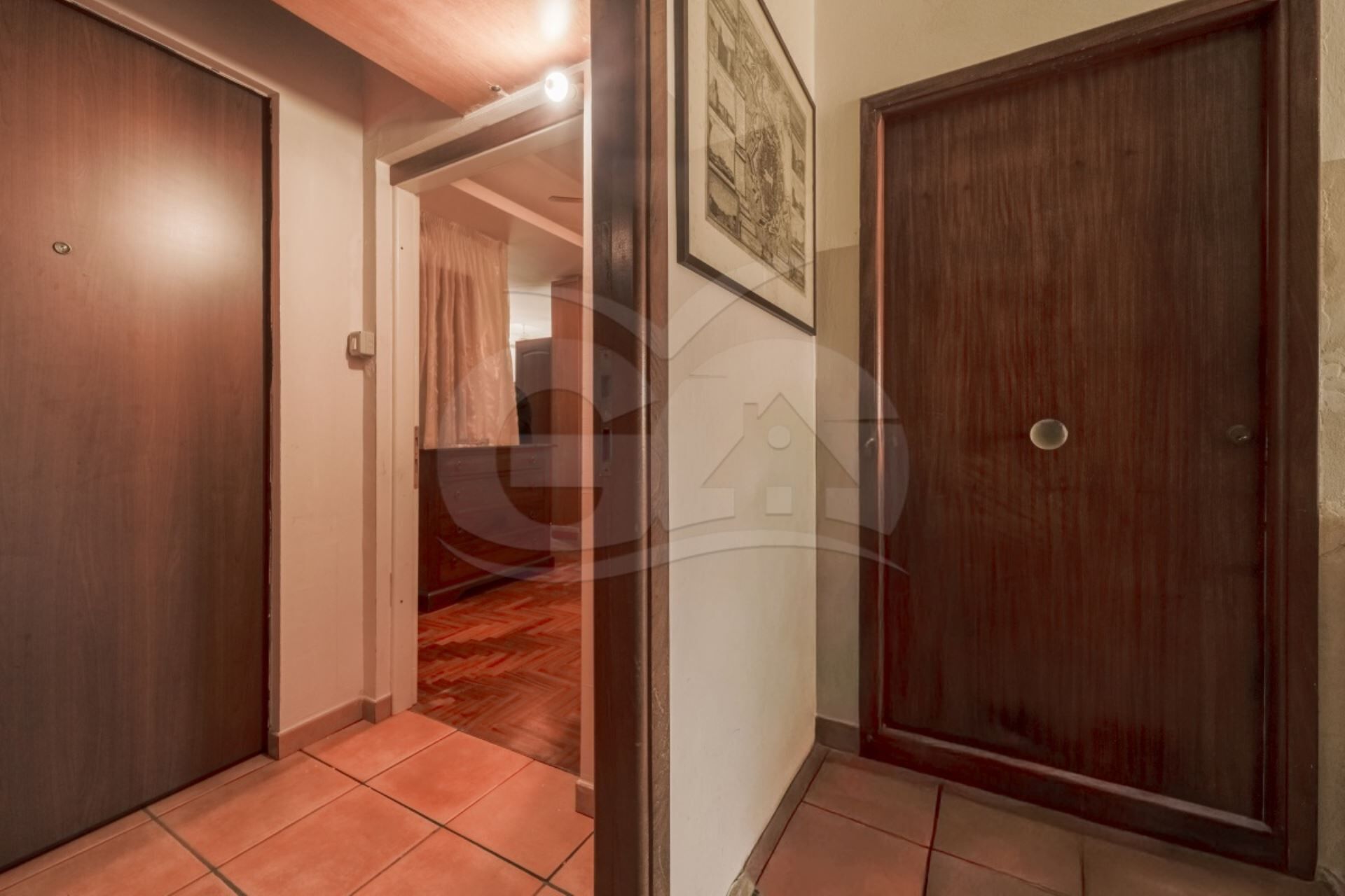 Un corridoio con porte in legno, pavimento piastrellato e un quadro appeso al muro.