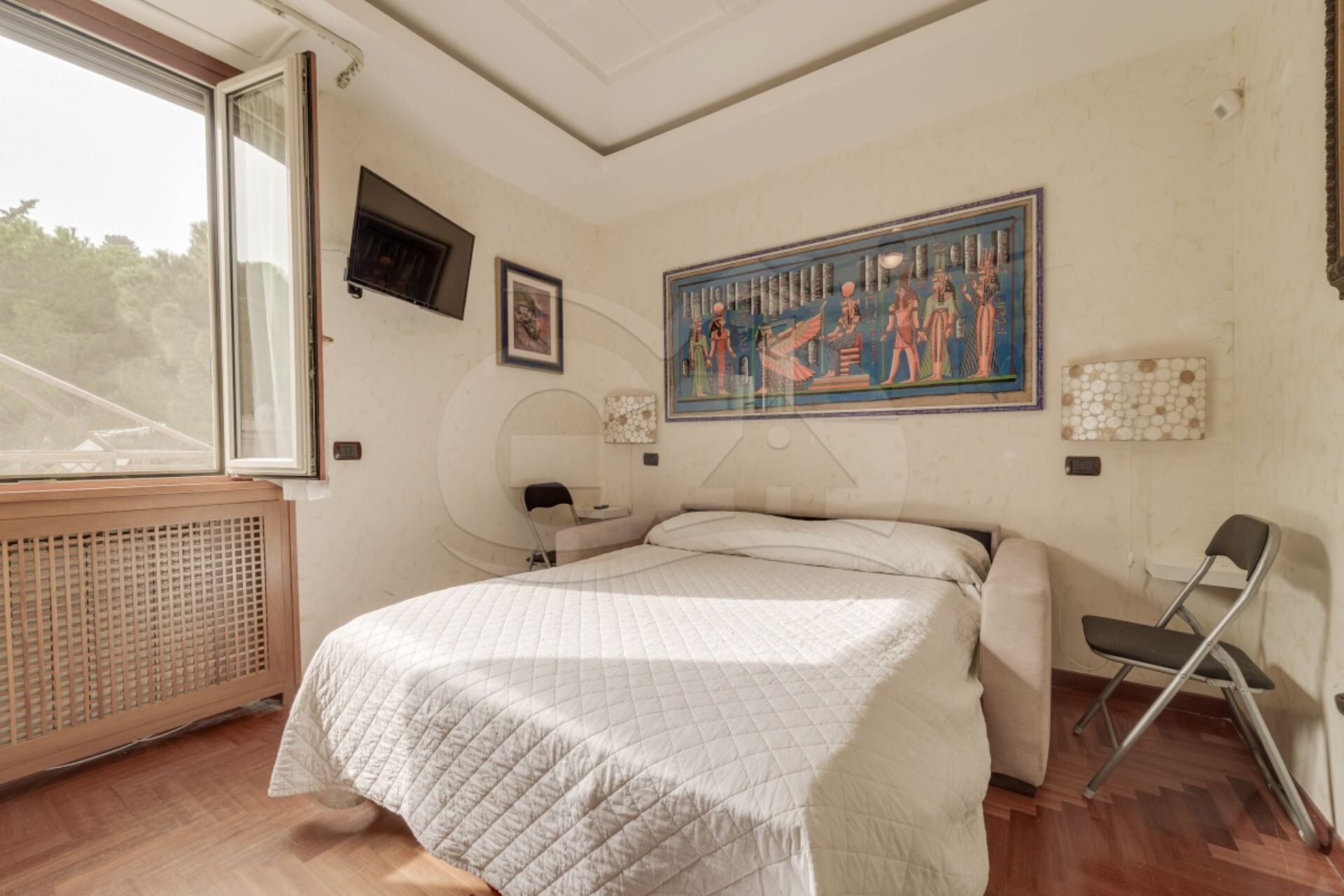 Ein Schlafzimmer mit Bett, Sessel, Heizkörper, Fenster und einem Bild an der Wand.