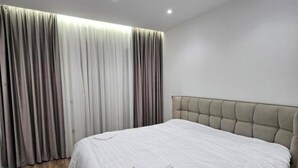 A modern hotel room with a large bed, a tufted headboard, and a set of curtains. - Najli apartments (Tiranë)