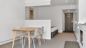 A modern, compact hotel room with a wooden dining table, white chairs, a bed, a small kitchenette, and an exit door. - Squatters Run 26 in the Heart of Thredbo (Thredbo)