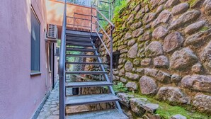 Una escalera metálica que sube hacia un edificio con un muro de piedra en un lateral.