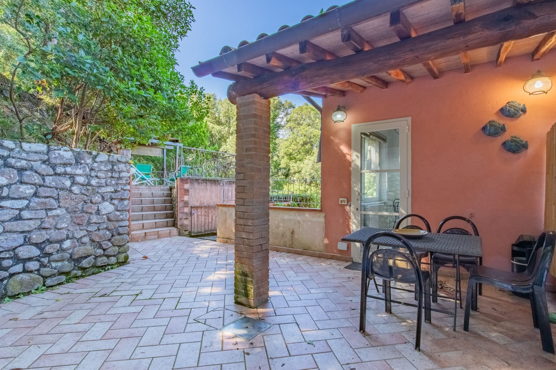 Un patio con escalones de piedra, una mesa con sillas y una pérgola de madera.
