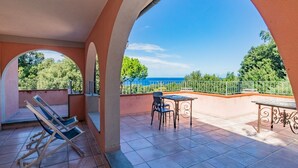 Un patio cubierto con una mesa y sillas, una silla plegable y vista al mar.