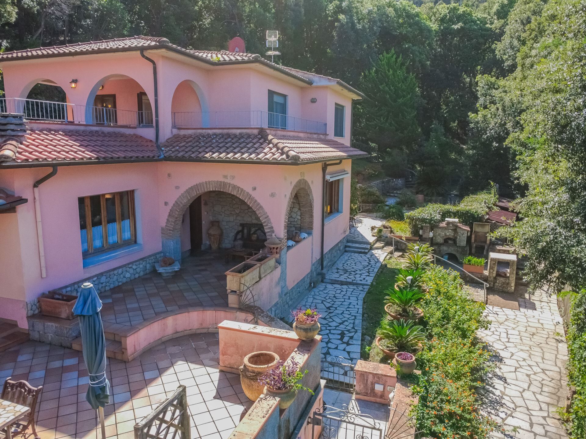 Une villa rose avec un toit en tuiles, des arches en pierre et une cour pavée agrémentée de plantes en pot.