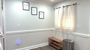 Una habitación con una pared blanca con paneles, un estante de madera con zapatos, un cesto de basura y tres marcos con citas inspiradoras.