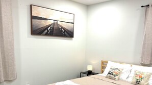 Una cama bien hecha con colcha color crema, un cojín con diseño floral y un cabecero.