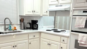 Una cocina con gabinetes blancos, una campana extractora de acero inoxidable, un horno empotrado y piso de madera.