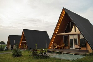 A modern A-frame cabin with a deck, outdoor seating, and large windows. - Aglamp.kz Almaty (Besqaynar)