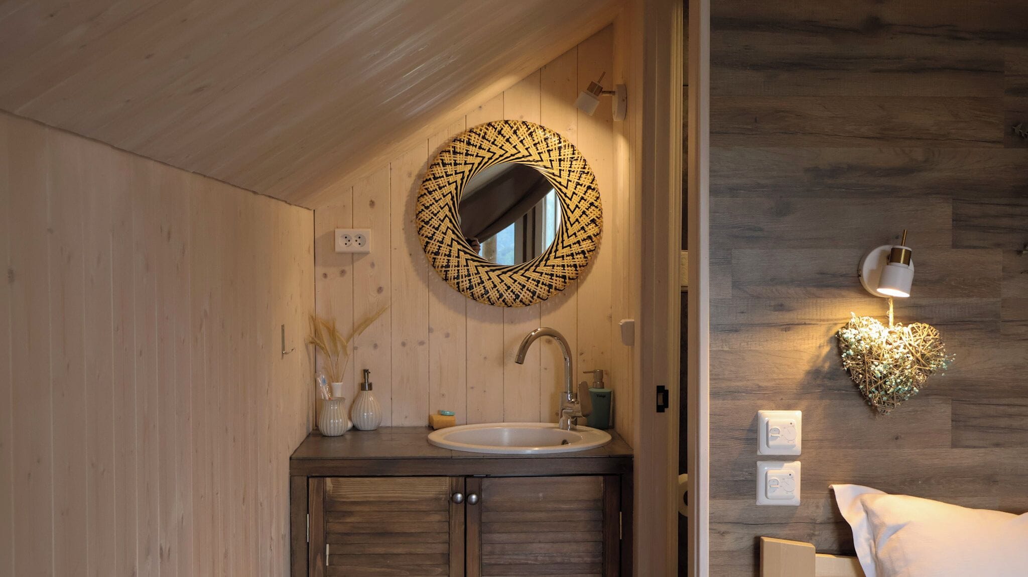 A wooden interior with a round mirror, a sink, and a wall-mounted light fixture.
