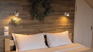 Una cama con ropa de cama blanca, dos lámparas fijadas a la pared y una corona en una pared de madera.