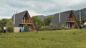 Dos cabañas modernas con techo triangular en un campo cubierto de hierba, con montañas al fondo.