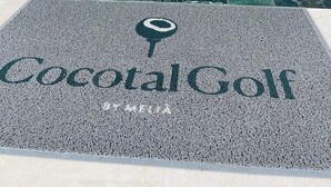 Un espace d’accueil avec un sol carrelé qui mène à un coin salon, une enseigne indiquant « Cocotal Golf » et des plantes en pot.
