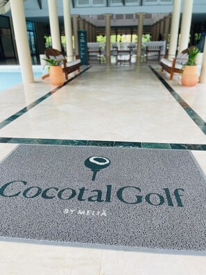 Ein Empfangsbereich mit gefliestem Boden, der zu einer Sitzecke führt, mit einem Schild mit der Aufschrift "Cocotal Golf" und Topfpflanzen.