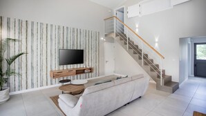 A modern living room with a sofa, TV, staircase, and a potted plant. - Perfect 3-bedroom house with AC in Rivière Noire District (Rivière Noire District)