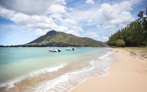 Ein Strand mit klarem Wasser, Booten und einem Berg im Hintergrund.