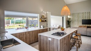 A modern kitchen with a central island, wooden cabinets, a gas stove, and a hanging light fixture. - Perfect 3-bedroom house with AC in Rivière Noire District (Rivière Noire District)
