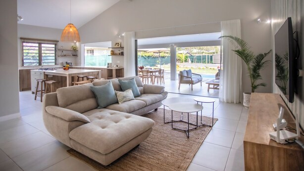 A spacious living area with a large sofa, a coffee table, and a TV mounted on the wall. - Perfect 3-bedroom house with AC in Rivière Noire District (Rivière Noire District)