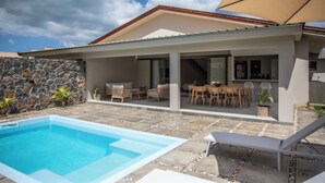 A modern house with a swimming pool, outdoor seating, and a stone wall. - Perfect 3-bedroom house with AC in Rivière Noire District (Rivière Noire District)