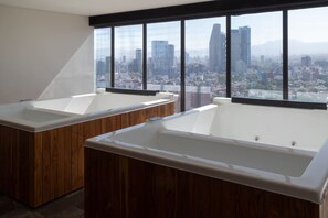 A modern bathroom with two large tubs, wooden cabinetry, and a cityscape view through large windows. - Casa Victoria a Pasos de Reforma (Ciudad de México)