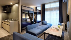 Una habitación de hotel compacta con kitchenette, sofá cama, mesa de comedor y televisor.