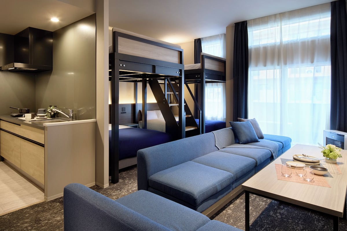 A compact hotel room with a kitchenette, a sofa bed, a dining table, and a TV.