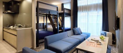 A compact hotel room with a kitchenette, a sofa bed, a dining table, and a TV.
