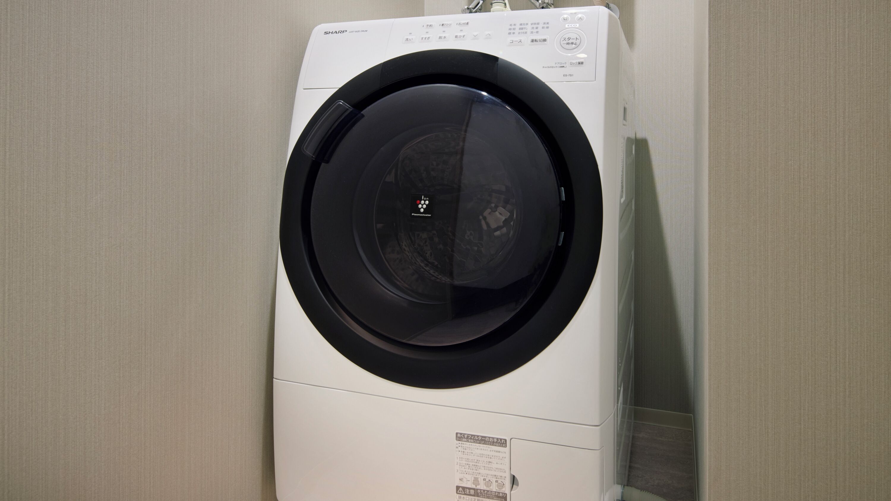 A front view of a white washing machine with a black door, control panel, and safety instructions.