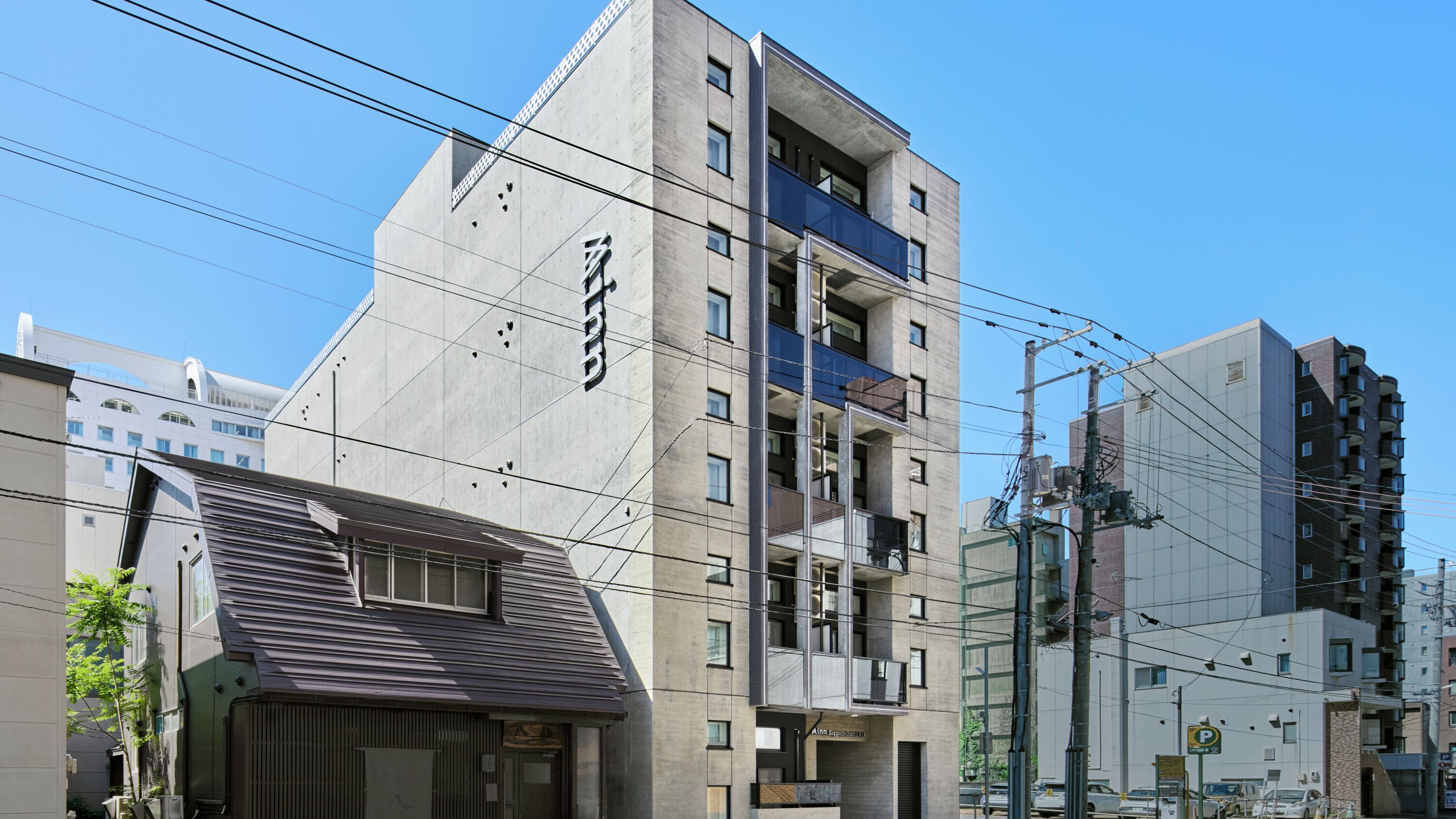 A multi-story building with a prominent sign, a balcony on the upper floor, and a parking sign nearby.