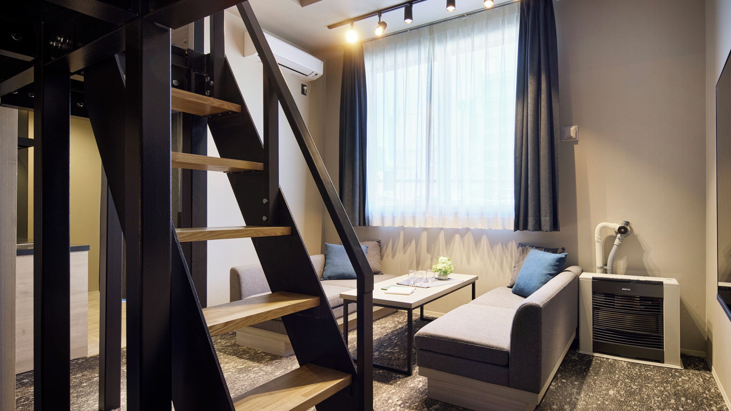 Una habitación moderna con una escalera, un sofá, una mesita y un radiador.