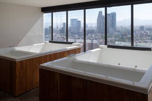 Ein modernes Badezimmer mit zwei großzügigen Badewannen, Holzschränken und Blick auf die Stadt durch große Fenster.