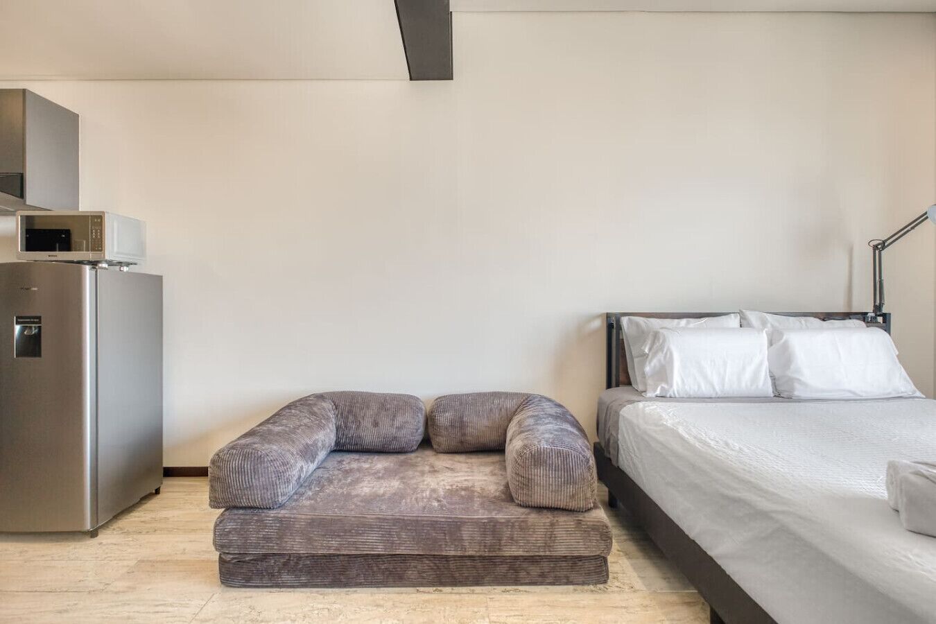 A modern hotel room with a bed, a sofa, a refrigerator, and a lamp.