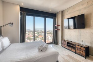 Ein modernes Hotelzimmer mit einem großen Bett, einem flachbildfernseher an der Wand und Blick auf die Stadt durch große Fenster.
