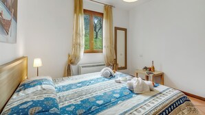A bedroom with a bed, a window with curtains, a bedside table with a lamp, and a radiator. - Residence La Perla - Apt 19 (Monte Isola)