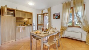 A compact kitchen with wooden cabinets, a dining table set for four, and a window with curtains. - Residence La Perla - Apt 19 (Monte Isola)