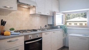 A modern kitchen with light wood cabinets, a gas stove, and a built-in oven. - Nuvolau Appartement Dolomites (Perarolo di Cadore)
