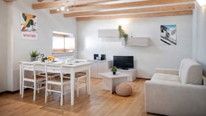 A modern living room with a dining area, wooden beams on the ceiling, a flat-screen TV, and a sofa. - Nuvolau Appartement Dolomites (Perarolo di Cadore)