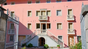 A pink building with a central staircase, multiple windows, and a gated entrance. - Nuvolau Appartement Dolomites (Perarolo di Cadore)