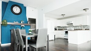 Eine moderne Küche mit weißen Schränken, einer schwarz-weißen Spritzschutzwand und einem Essbereich mit blauer Akzentwand und einer Uhr.