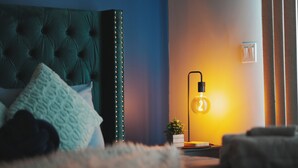 Ein Schlafzimmer mit einer gesteppten Kopfteile, einer Nachttischlampe, einer kleinen Pflanze und einem flauschigen Teppich.